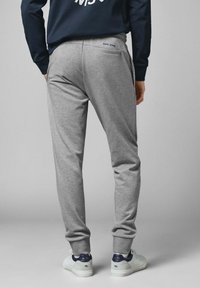 Grå sweatpants med en åtsittande passform, tillverkade av bomullsblandat tyg, med sidofickor och en logodetalj på baksidan. Vita sneakers.