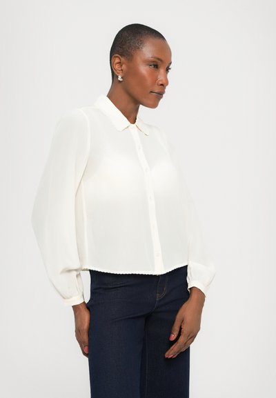 Valge, kerge bluus kraega, nööpidega esiosas ja pikkade puffvarrukatega. Hemline on veidi lühem. Sile tekstuur.
