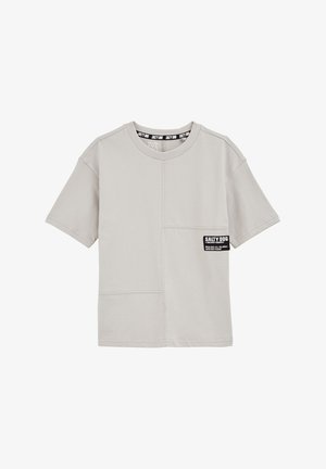 Svetlo siva kratkosleeva majica s okruglim izrezom, s preklopnom džepom i crnom oznakom "Salty Dog" sprijeda. Glatka tekstura tkanine.