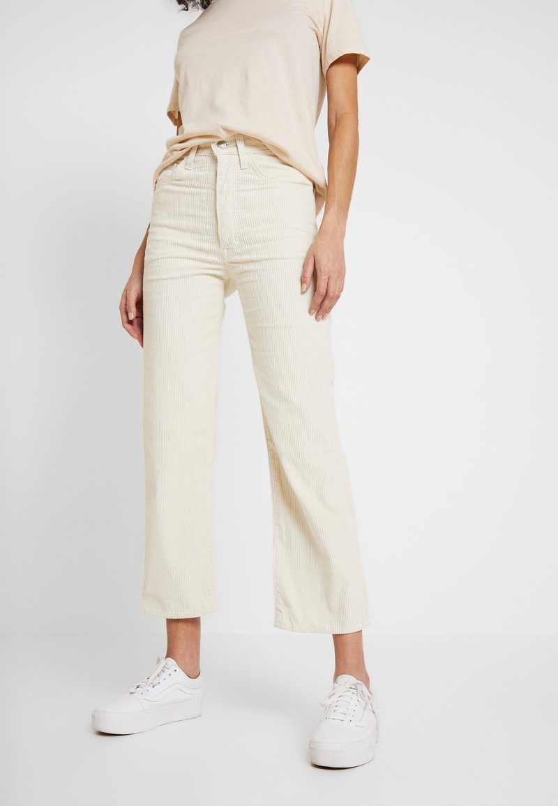 Krämsfärgade kordfloth vida byxor med hög midja, försedda med knappstängning och framfickor, tillsammans med en ljusbeige t-shirt och vita sneakers.