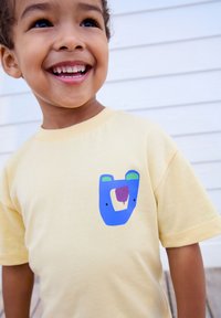 Yellow short-sleeve t-shirt featuring a blue bear face design with green ears and a purple snout, made from soft cotton material.