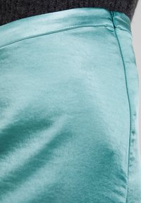 En närbild av en turkos sidentubkjol med en jämn textur, en lätt glänsande yta och noggrant stygn längs midjebandet.