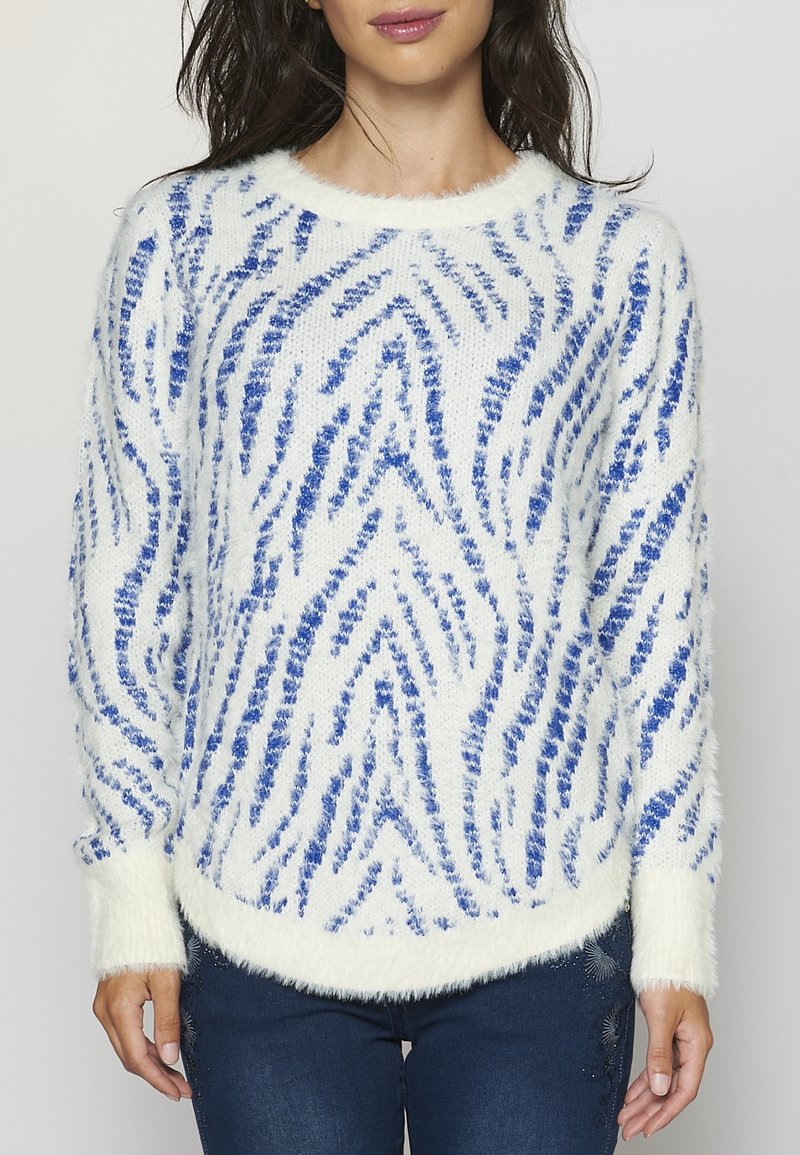 White fuzzy sweater with blue zebra stripes, round neckline, and ribbed cuffs. Soft texture with a slightly curved hem. Paired with denim.