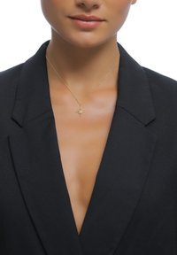 Goldener Sternanhänger mit einer strukturierten, achtzackigen Sternform an einer feinen Kette, getragen zu einem tief ausgeschnittenen schwarzen Blazer.