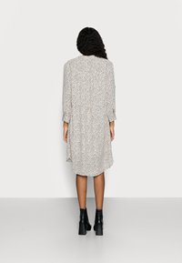 Hellbeiges Kleid mit schwarzen Sprenkeln, lockere Passform, geknöpfte Manschetten und geschwüngem Saum. Kombiniert mit schwarzen klobigen Stiefeletten mit Absatz.