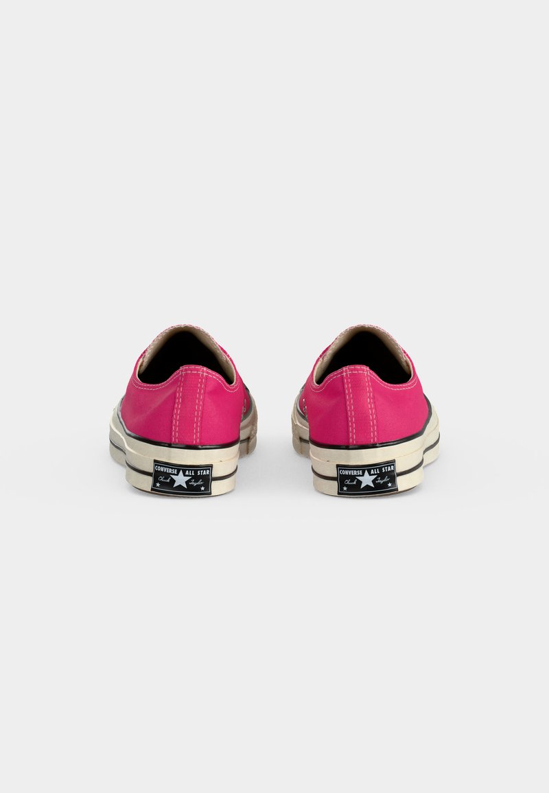 Paar rosa niedrig geschnittene Converse All Star Sneakers von hinten auf weißem Hintergrund.