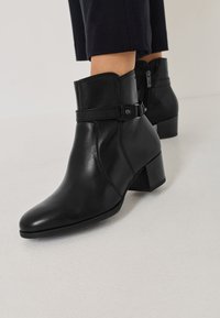 Melnas ādas potītes botas ar smailu pirkstu, ar sānu rāvējslēdzēju un regulējamu siksniņu ar sprādzi. Bloku papēdis.