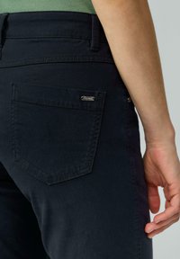 Pantalons en coton bleu marine avec une poche à rabat et un détail en métal au niveau du logo. Le tissu a une texture lisse et un design à coupe regular.