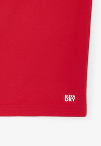 Röd sporttröja med texturerat tyg, korta ärmar och en vit "ULTRA DRY"-logotyp tryckt nära fållen.