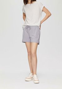 Světlé šedé šortky s elastickým pasem a šňůrkou, v kombinaci s proužkovaným bílým a levandulovým tričkem s krátkým rukávem. Tenisky v neutrálních tónech.