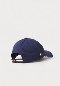 Mørkeblå baseballkasket med en buet skygge, justerbar rem og en stribet detalje i rød og hvid. Mærkets logo-patch på siden.