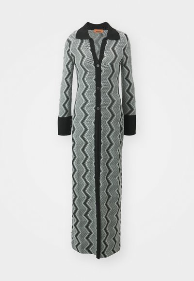 Lång kofta med ett svart och vitt zigzag-mönster, med svart krage och muddar, samt knappstängning framtill. Strukturerad stickad tyg.