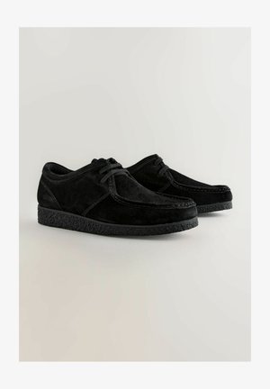 Sorte ruskindsko med lav profil, rund tå, kontrasterende syninger og struktureret gummisål. Snørebånd sikret foran.