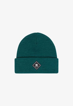 Un bonnet tricoté teal en matériau doux. Il présente un revers replié et une patch logo en forme de diamant noir avec du texte blanc, mesurant environ 24 cm de hauteur.