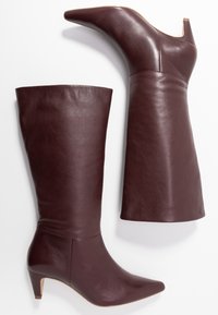 Bottes en cuir bordeaux à talons, avec un bout pointu et une texture lisse. Comprend une tige haute et un design de talon modeste.