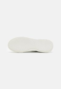 Witte sneakerzool met een gestructureerd patroon, met een golfontwerp, afgeronde randen en een reliëfmerklogo nabij de hiel.