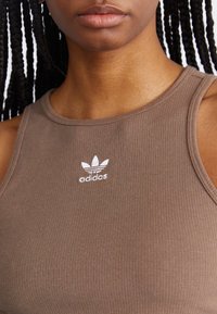 Brun ribbad linne med en vit broderad Adidas-logotyp på bröstet. Designen har en rund hals och breda axelband.