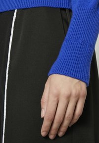 Blå ribbad tröjärm som är kombinerad med ett svart plagg med en vertikal vit rand. Tyget verkar mjukt och något strukturerat.