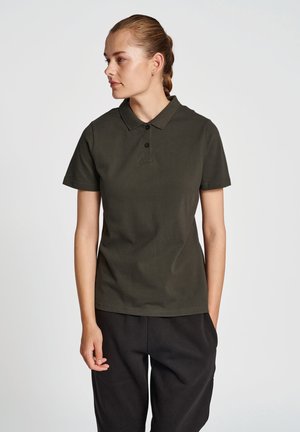 Donkergroen polo met een kraag, twee knopen, en korte mouwen, gedragen met losse zwarte broek. Een gladde katoenstof.
