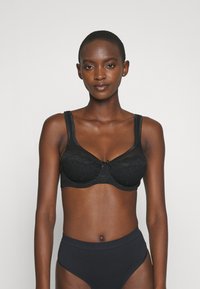 Svart spetsbh med mjuk underwire-design, breda axelband och en rosett i mitten. Bärs med högmidjade svarta trosor.