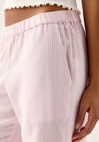 Pantaloni in tessuto rosa chiaro a righe, con una texture morbida, vita elastica e tasche laterali, caratterizzati da sottili strisce bianche e grigie.