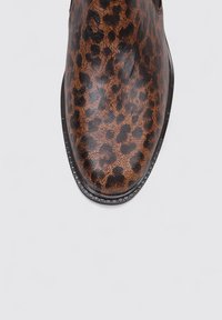 Botín de tobillo con estampado de leopardo, acabado en cuero suave, punta redonda y suela de goma negra. Presenta costuras sutiles a lo largo del borde.