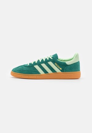 Zapatilla verde de Adidas con franjas beige, parte superior de ante, suela de goma y marca "Spezial" en dorado en el lateral.