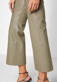 Khaki leren culottes met een soepele textuur, wijde broekspijpen en zichtbare naden. Aangevuld met sandalen met banden en versieringen.