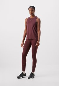 Bordó atlétikai trikó és leggings szett, sima felülettel és fehér Nike logóval. Feketében viselt sportcipővel.