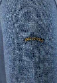 Maglione blu lavorato a maglia con un motivo testurizzato e un logo ricamato "PAUL & SHARK" in oro su uno sfondo blu scuro.