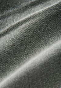 Tejido de denim en un tono gris, con una superficie texturada y ligeramente áspera, que presenta un patrón de tejido en diagonal y arrugas naturales.