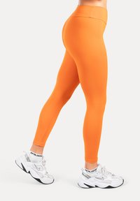 Orange leggings med hög midja i stretchigt tyg med en jämn yta. Matchade med vita klumpiga sneakers och vita strumpor.