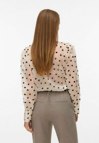 Prozirna krema bluzica s crnim uzorkom srca, napuhanim ramenima i rukavima s gumbima, uparena sa svijetlosivim tapered hlačama.