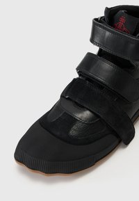 Zwarte sneaker met een combinatie van leer en suèdine materialen. Het ontwerp bevat dubbele klittenbandsluitingen, een getextureerde neuskap en een gumrubberen zool.