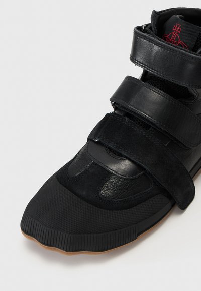 Sorte joggesko med en kombinasjon av lær og semsket skinn. Designet inkluderer to borrelåsremmer, teksturert tåhette, og en gummisåle.