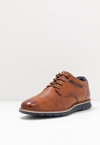 Chaussure en cuir marron à lacets avec une texture lisse, bout rond, semelle noire contrastante et détail de logo subtil sur le côté.