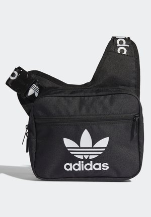 Sac bandoulière noir Adidas avec poche zippée avant et logo trèfle blanc avec texte. Sangle réglable avec boucle brandée.