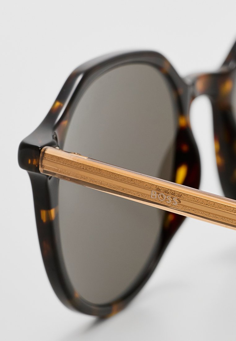 Lunettes de soleil écaille de tortue avec verres teintés, dotées d'un accent en métal doré sur les branches gravé de "BOSS". Détails de surface texturée.
