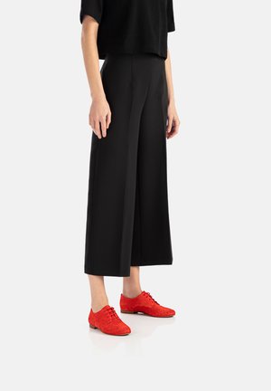 Pantalones anchos negros combinados con zapatos de ante rojo brillante que presentan detalles perforados y cordones. Diseño simple y moderno con líneas limpias.