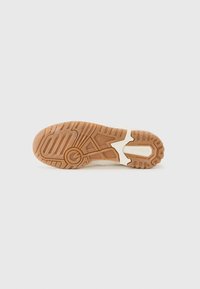 Ljusfärgad sneakersula med mönstrad gummi för grepp; har skåror och rännor för flexibilitet, med en logga i hälområdet.