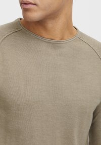 Beżowy sweter dzianinowy z okrągłym dekoltem, z teksturowanym materiałem i lekko dopasowanym krojem. Widoczne szwy na ramionach.