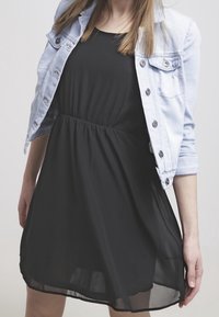 Musta ilmanhiha dressi, jonka vyötärö on gathered-tyylinen, yhdistettynä vaaleaan farkkutakkiin, jossa on nappikoristelu ja käärityt hihat.