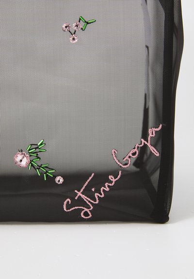 Sort mesh tote med broderede blomster i pink og grøn, med navnet "Stine Goya" i pink tråd i bunden.