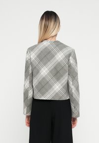 Giacca cropped a quadri grigia con maniche lunghe, caratterizzata da un tessuto testurizzato e dettagli bianchi in un design strutturato.