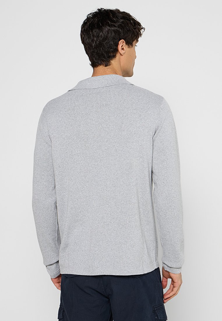 Polo grigio a maniche lunghe con colletto, realizzato in un morbido tessuto testurizzato. Presenta una vestibilità rilassata e una cucitura discreta lungo le cuciture.