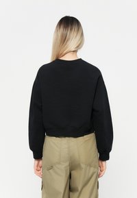 Must jaotatud mikrofliisiga sweatshird, millel on ümmargune kaelus ja pikad varrukad, koos helesiniste cargo-pükstega, millel on õmblustega detailid ja taskud.