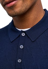 Polo navy con un motivo testurizzato, colletto a coste e patta con tre bottoni dotata di bottoni decorativi.