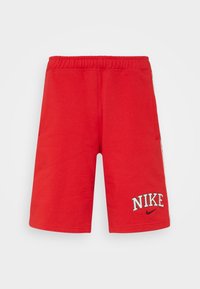 Červené sportovní šortky vyrobené z měkké tkaniny, s elastickým pasem, bočními kapsami a vyšitým logem "NIKE" na přední straně.