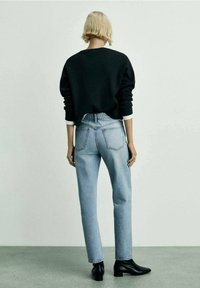 Pull noir court à manches longues, associé à un jean taille haute bleu clair et des bottines noires. Vue arrière simple et épurée.