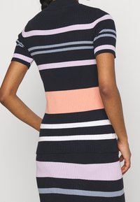 Ribattu neulemekko lyhyillä hihoilla, jossa on vaakasuoria raitoja tummansinisessä, laventelissa, persikassa ja valkoisessa. Istuva siluetti, jossa on pikeepaita-tyylinen kaulus.